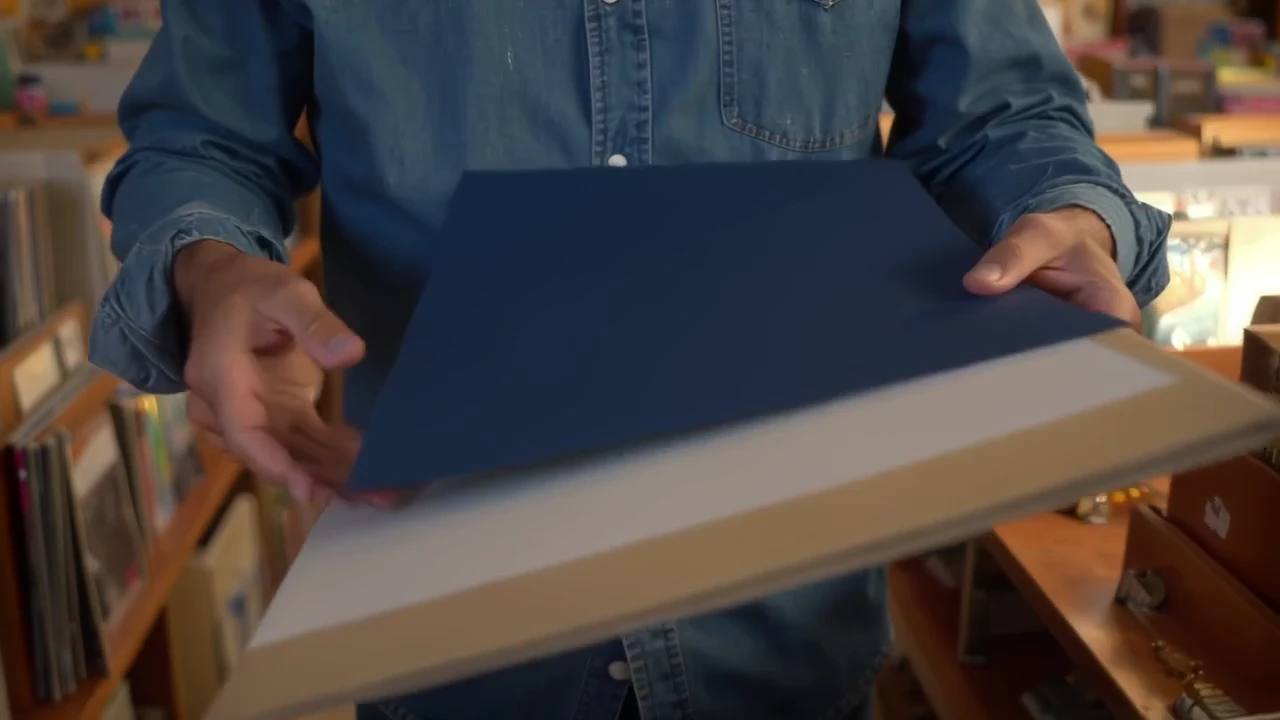 A record-shop owner chooses a sleeve and speaks to camera before the scene moves to a turning record. Two original shots become a 20-second film with native speech and a generated soundtrack.